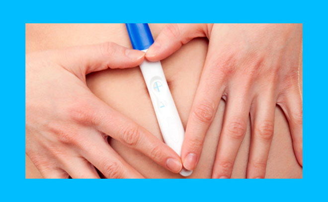 женщина держит руки в виде сердца на своем животе с положительным тестом на беременность
