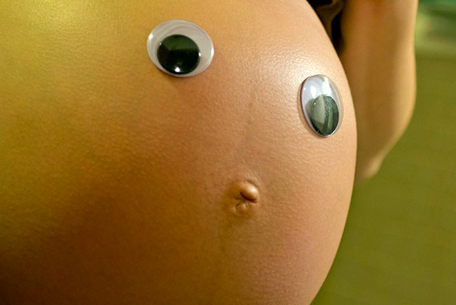 живот беременной женщины с накладными глазами