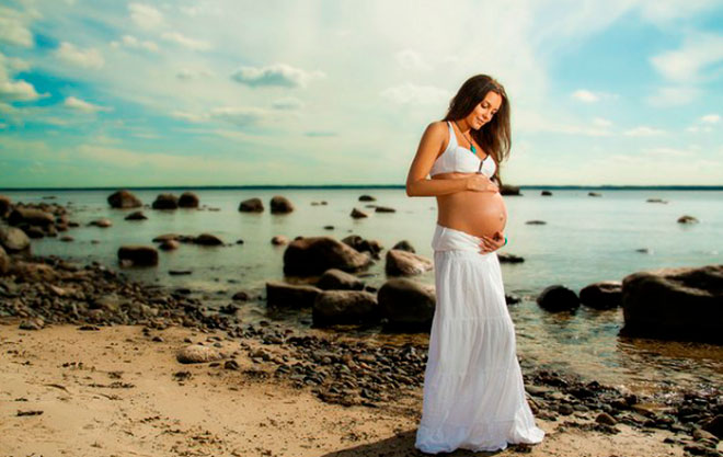 беременная женщина в длинном платье на берегу моря