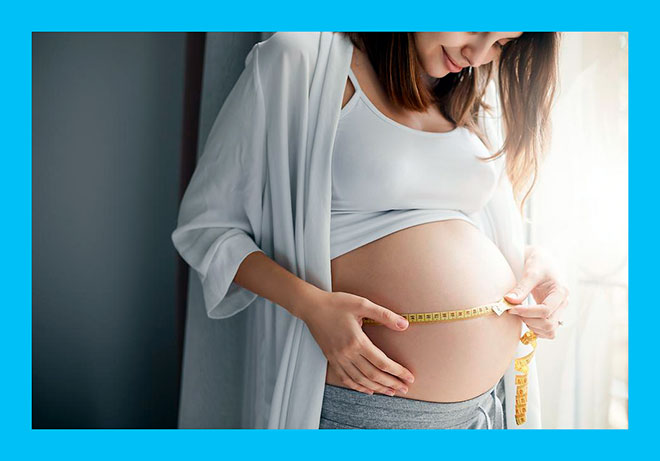 беременная женщина измеряет свой большой живот метром